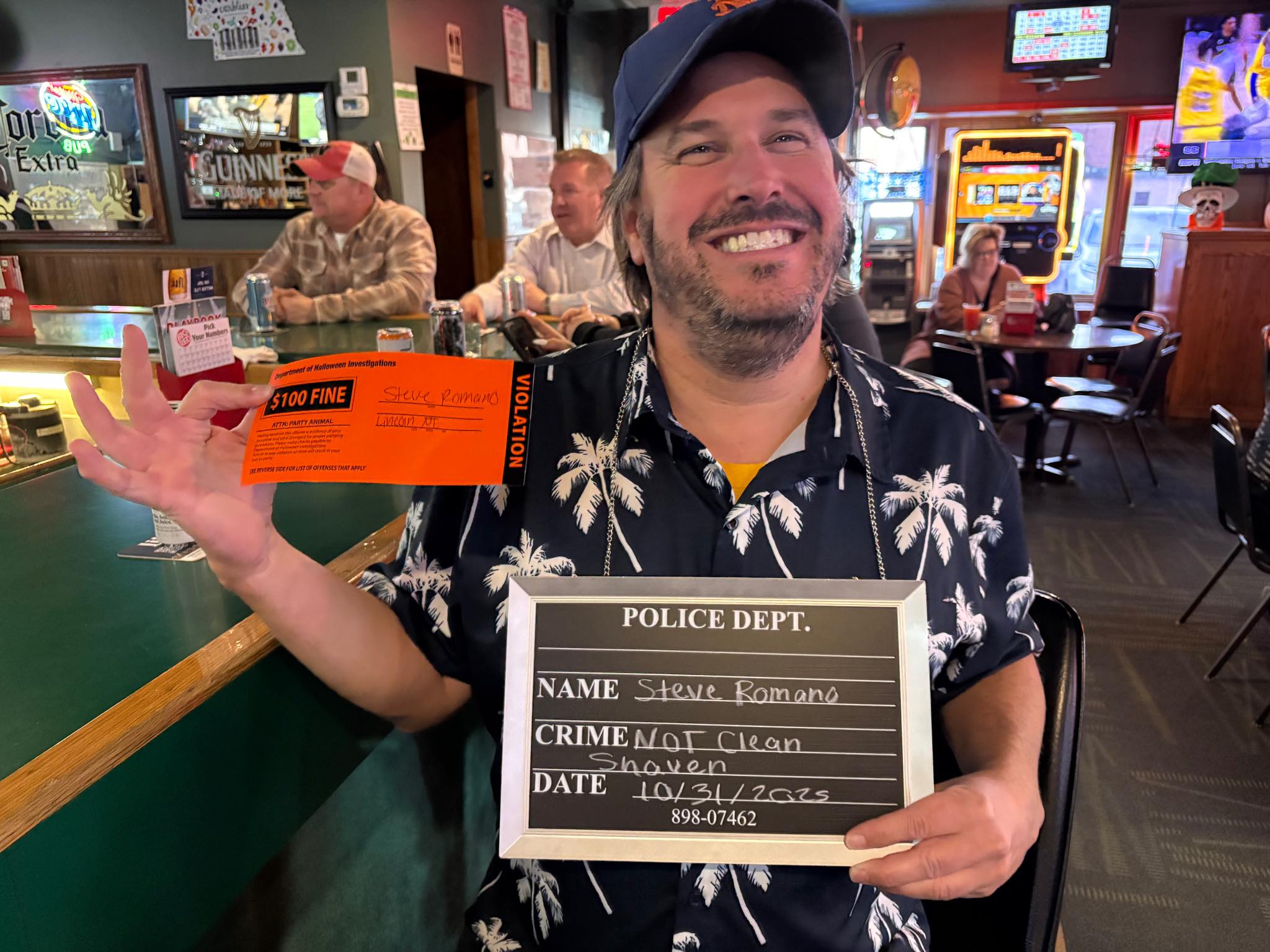 Steve smiling in a bar while holding an orange citation and a police department sign.